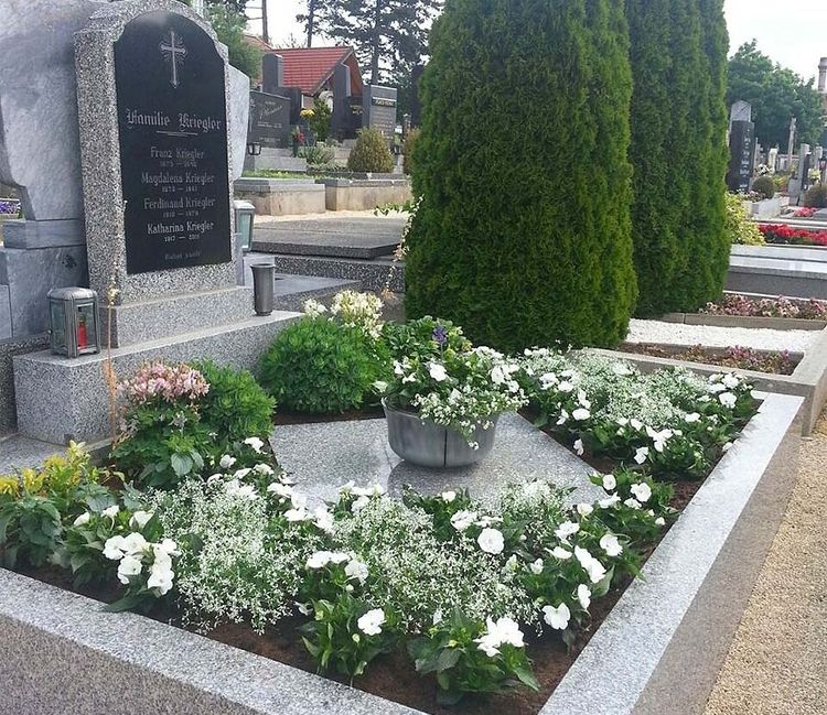 Ein Grab mit Grabstein und Grabschmuck in Form verschiedener Blumen und Pflanzen