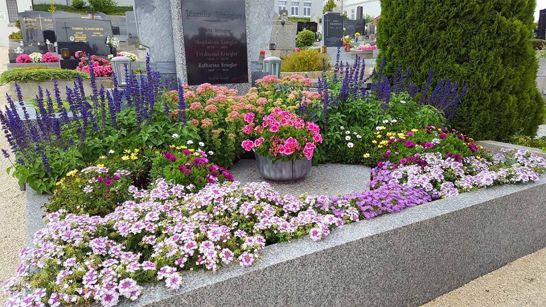 Ein Grab mit Grabstein und viel Grabschmuck in Form von verschiedenen Blumen und Pflanzen