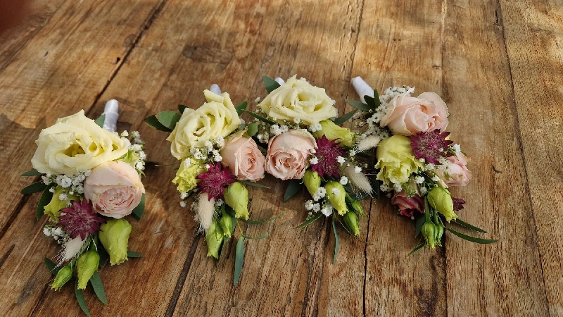 Drei kleine Blumenarrangements liegen nebeneinander auf Holz. Sie sind für Anzug oder Jackett gedacht und wirken elegant und dezent.