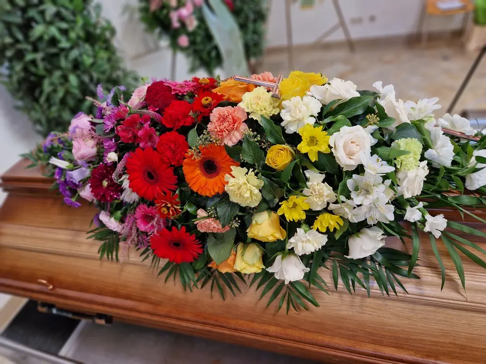 Blumenschmuck auf Sarg, bestehend aus bunten Frühlingsblumen in Rot, Gelb, Orange und Weiß. Blumenkranz für Beerdigung